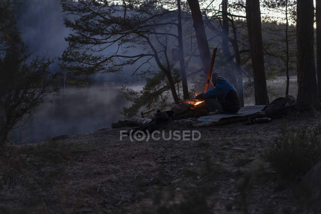 Teenage boy by campfire at sunset by Oxsjon lake in Lerum, Sweden — Stock Photo
