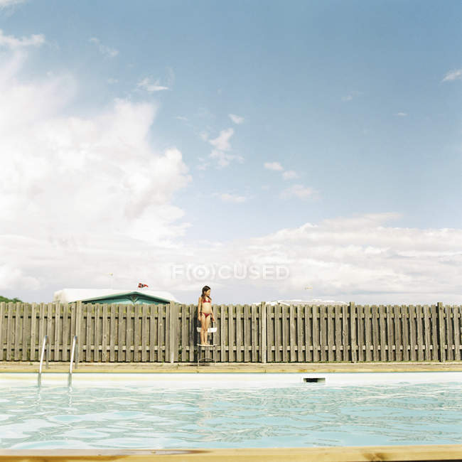 Menina em pé na cadeira por piscina — Fotografia de Stock