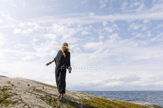 Mujer barrida por el viento vistiendo negro de pie sobre roca - foto de stock