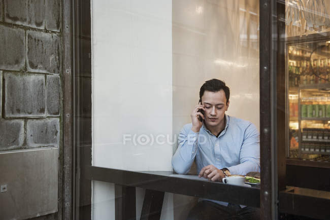 Молодий чоловік сидить і розмовляє по мобільному телефону в кафе — стокове фото