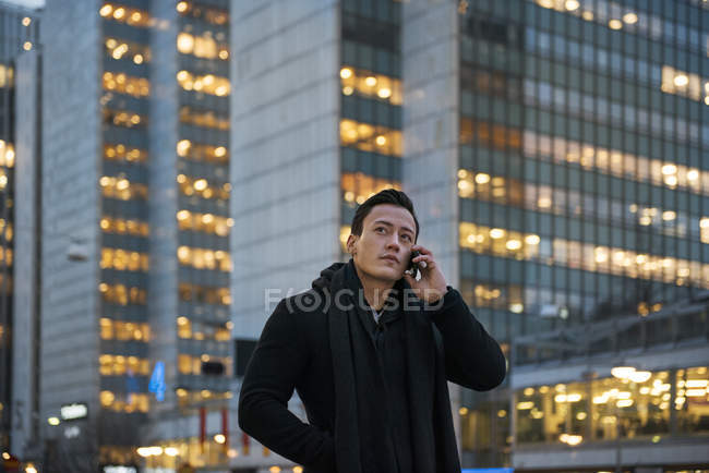 Young man talking on cell phone while walking down city street — Stock Photo
