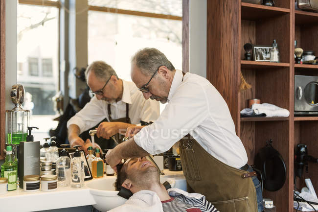 Парикмахер, моющий волосы молодого человека, избирательное внимание — стоковое фото