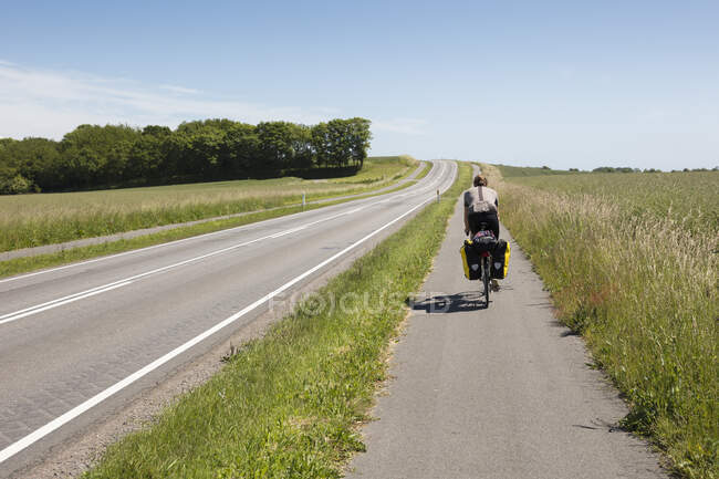 Uomo in bicicletta per strada rurale, vista sul retro — Foto stock
