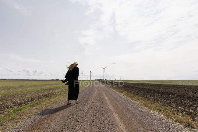 Femme portant noir marchant sur la route rurale — Photo de stock