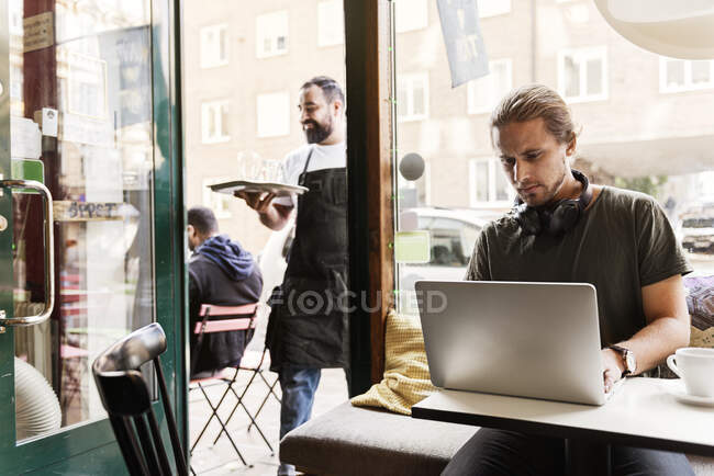Young man working on laptop in cafe — Stock Photo