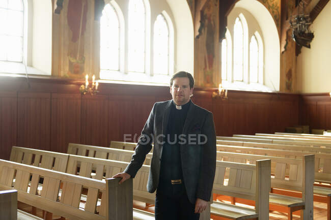 Retrato del sacerdote de pie y mirando a la cámara en la iglesia - foto de stock
