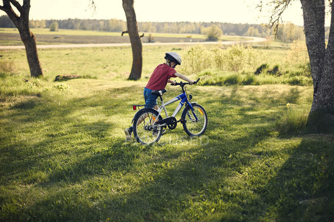 Хлопчик штовхає велосипед на газон, вибірковий фокус — стокове фото