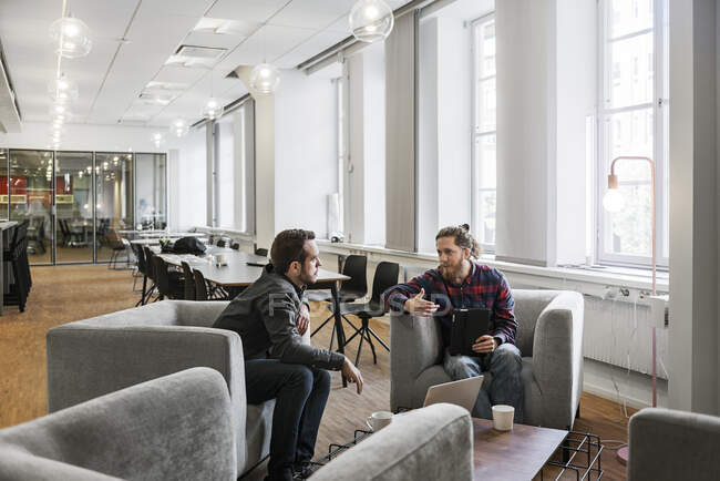 Coobreiros masculinos focados sentados e falando no escritório — Fotografia de Stock
