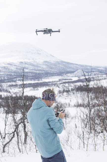 Hombre que usa aviones no tripulados en montañas nevadas - foto de stock