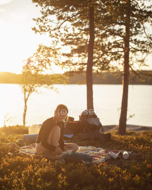 Молодая женщина, читающая на закате у озера Норра-Бредсьон, Швеция — стоковое фото