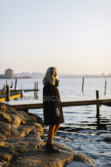 Frau steht bei Sonnenuntergang auf Felsen am Meer — Stockfoto