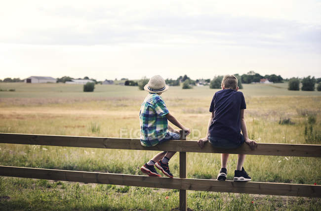 Boys sitting on fence in front of pasture — Stock Photo