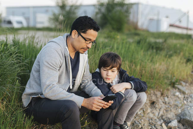 Pai e filho usando um telefone inteligente na grama — Fotografia de Stock