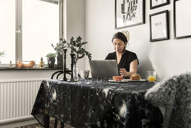 Молода жінка використовує ноутбук під час сніданку — стокове фото