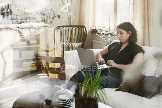 Молода жінка використовує ноутбук на дивані, вибірковий фокус — стокове фото