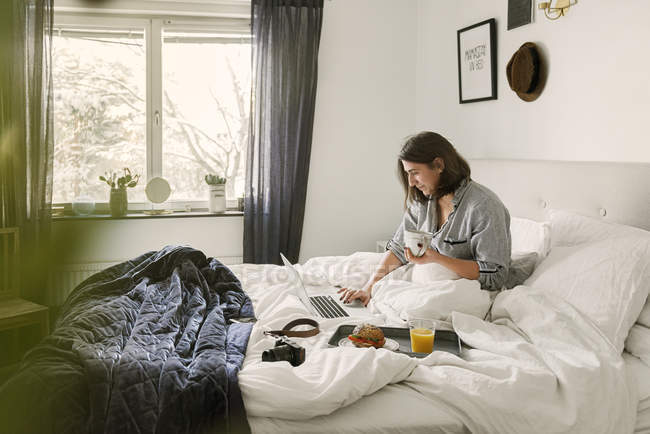 Mujer joven usando portátil en la cama - foto de stock