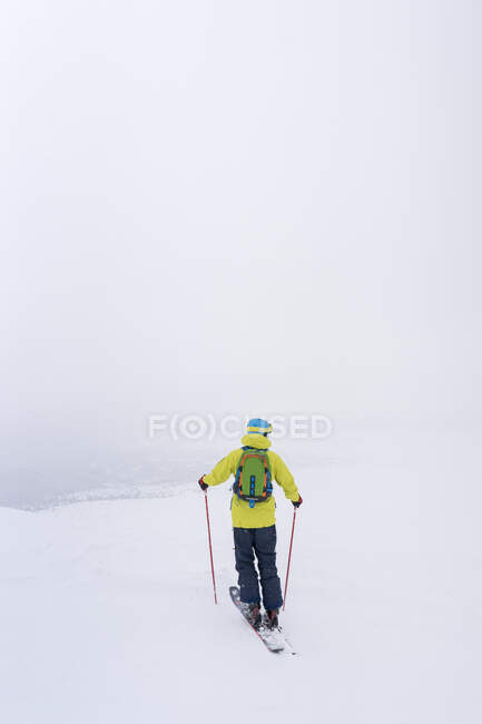 Вид сзади человека с рюкзаком, катающегося на лыжах в заснеженных горах — стоковое фото