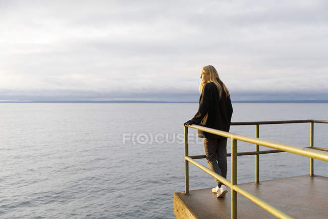 Jeune femme penchée sur la rampe au-dessus du lac — Photo de stock
