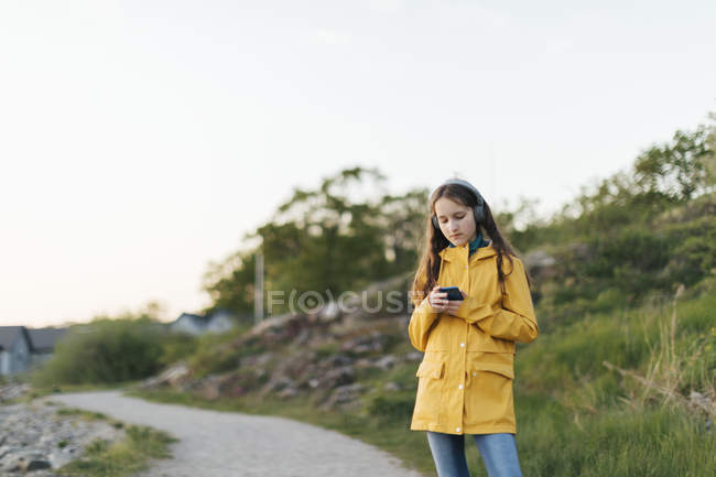 Girl wearing yellow coat and using smart phone in park — Stock Photo
