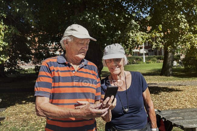 Portrait d'un couple d'aînés heureux utilisant un téléphone intelligent à l'extérieur par une journée ensoleillée — Photo de stock