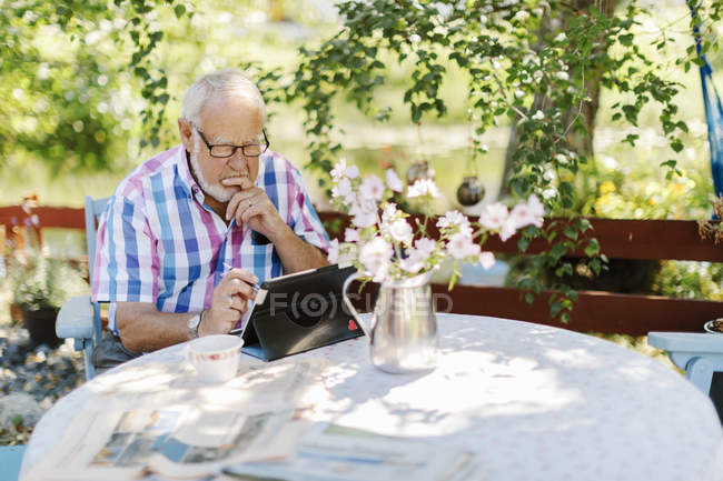 Homem sênior usando tablet digital na mesa ao ar livre — Fotografia de Stock