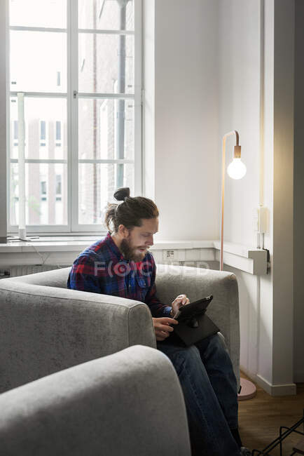 Зосереджений молодий чоловік використовує планшетний ПК, сидячи за лампою — стокове фото