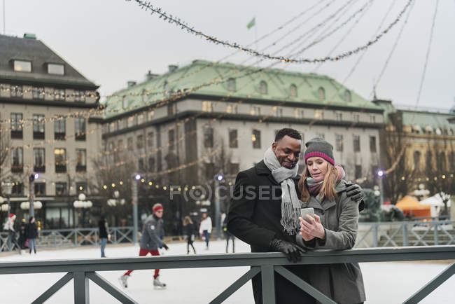 Casal usando telefone inteligente na pista de gelo, foco seletivo — Fotografia de Stock