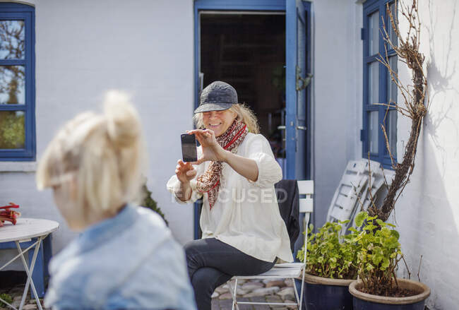 Woman photographing her daughter with smartphone in backyard — Stock Photo