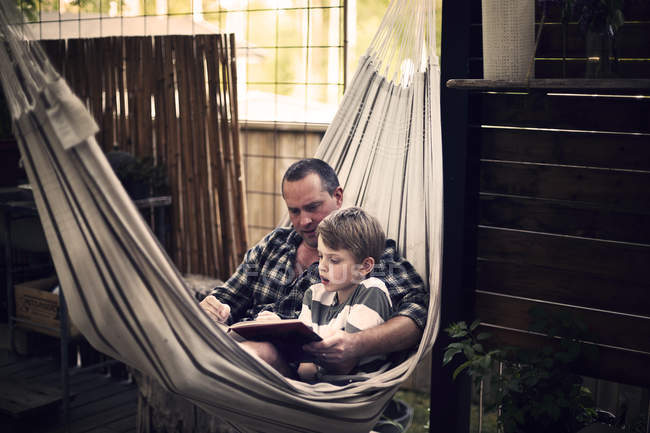 Homme adulte moyen et garçon lisant dans l'hamac — Photo de stock