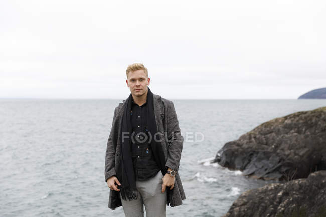 Hombre joven con abrigo gris junto al lago Vattern en Stora Lund Nature Reserve, Suecia - foto de stock