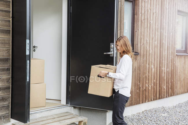 Woman carrying cardboard box into house — Stock Photo