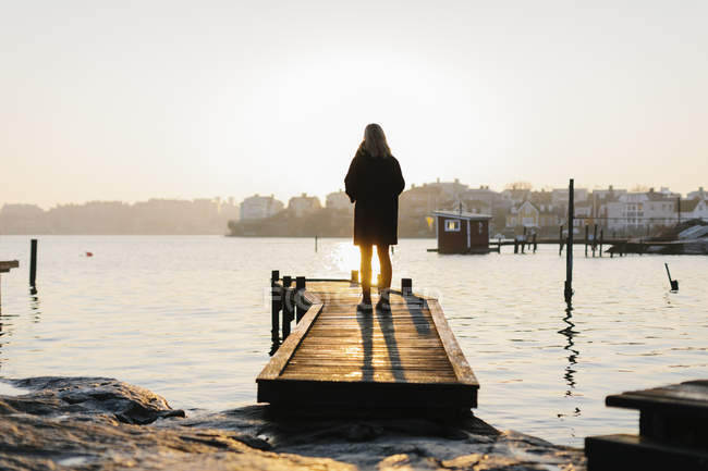 Silhouette of woman standing on jetty at sunset — Stock Photo
