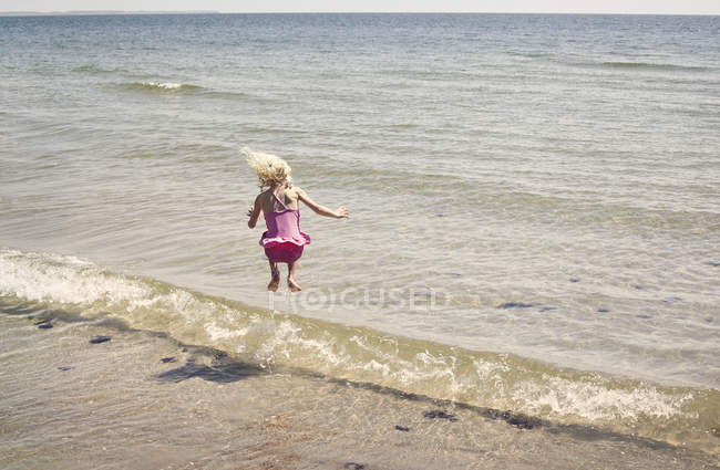 Girl jumping in waves on beach — Stock Photo