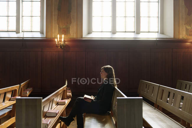 Sacerdote con Biblia sentado en el banco de la iglesia - foto de stock