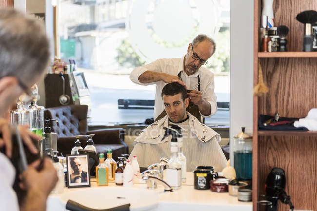 Reflexión sobre la cortina que corta el cabello de los hombres jóvenes en espejo - foto de stock
