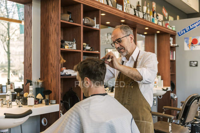 Парикмахер стрижет волосы молодого человека, избирательный фокус — стоковое фото