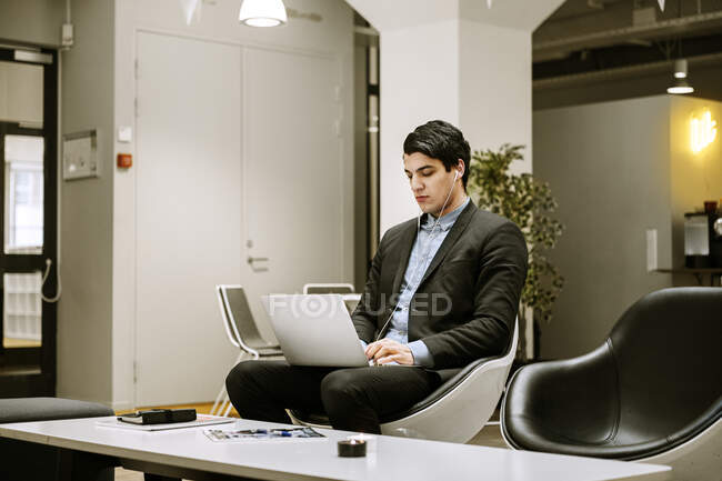 Young man in earphones using laptop in office — Stock Photo