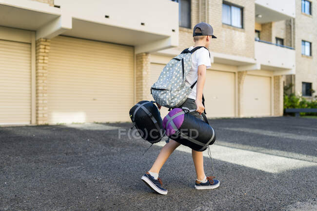 Garçon portant un sac à dos tenant un sac de couchage — Photo de stock