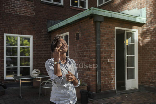 Mulher sorrindo e tendo em telefonema perto de casa — Fotografia de Stock