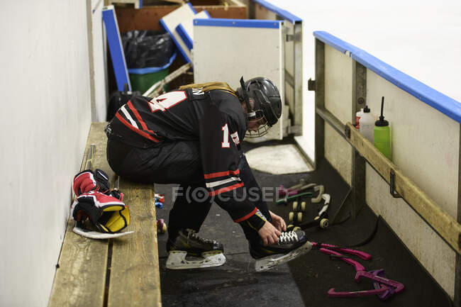 Ragazza in uniforme da hockey su ghiaccio allacciatura lacci su pattini da ghiaccio — Foto stock