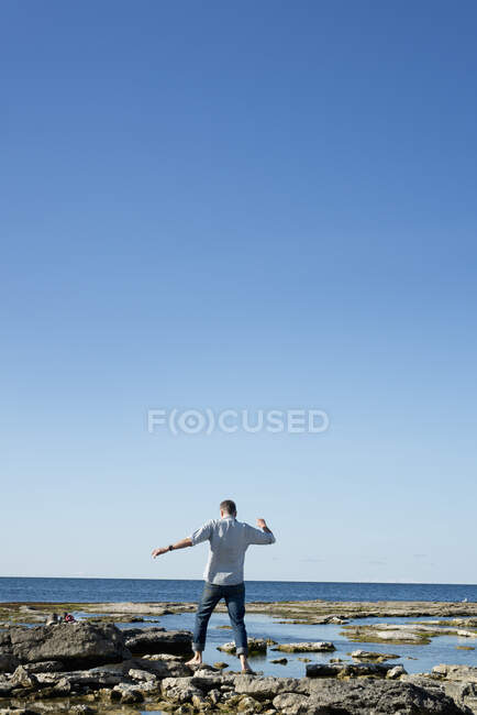 Man walking barefoot on rocks by sea, back view — Stock Photo