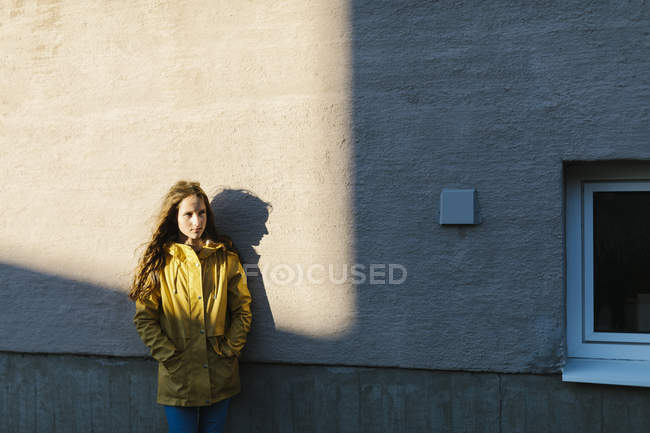 Девушка в жёлтом плаще у стены — стоковое фото