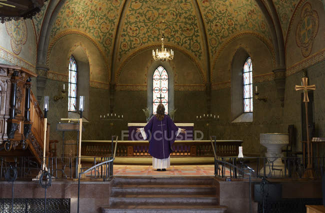 Sacerdote con túnicas púrpura de pie en el presbiterio de la iglesia - foto de stock