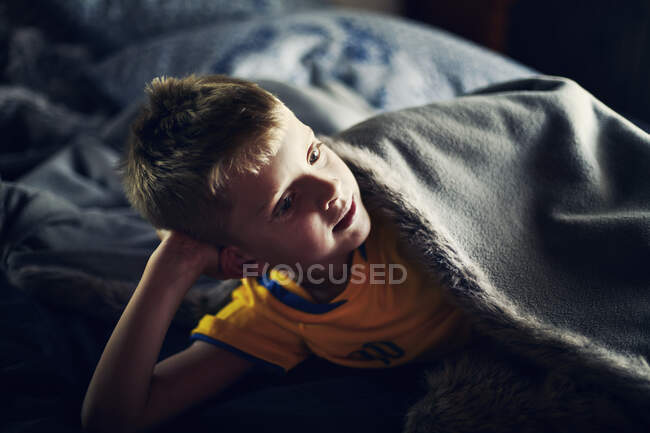 Хлопчик лежить під ковдрою на ліжку — стокове фото