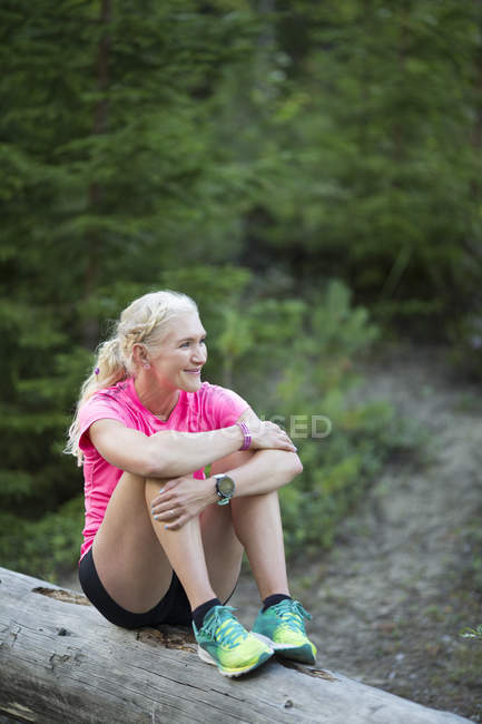 Frau lächelt auf Baumstamm im Wald — Stockfoto