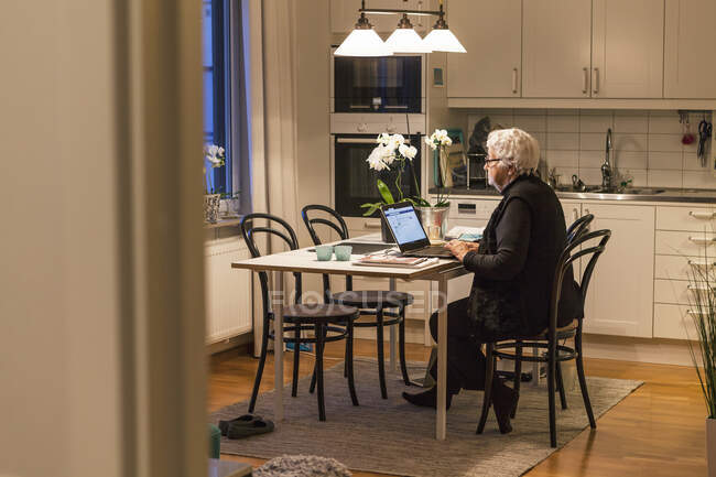 Старша жінка використовує ноутбук на кухні — стокове фото