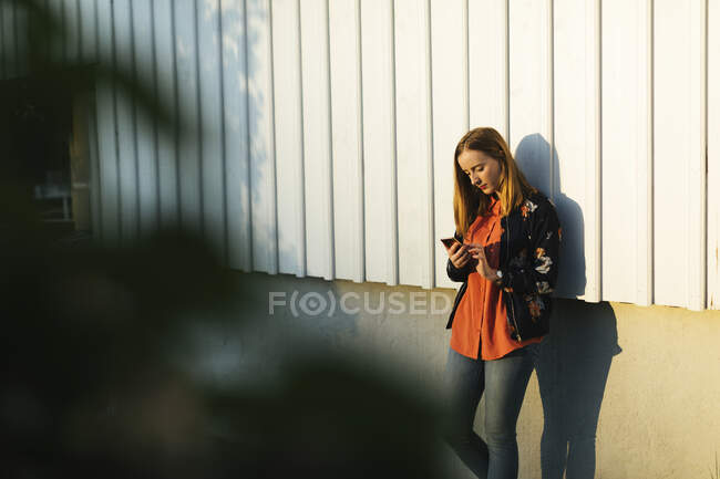Junge Frau nutzt Smartphone an Wand — Stockfoto