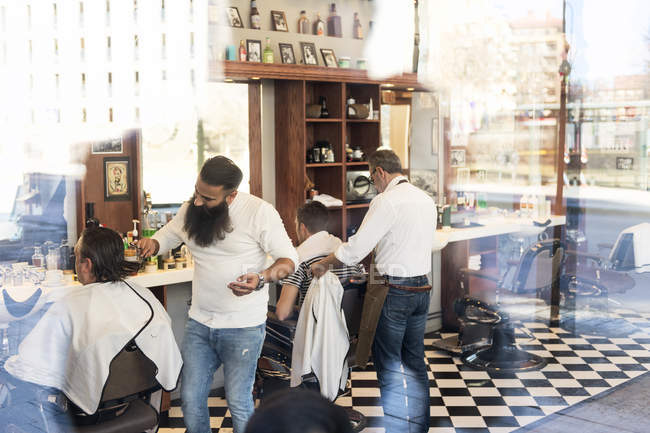 Vue à travers la fenêtre de barbiers coupant les clients cheveux — Photo de stock