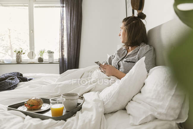 Молода жінка використовує смартфон у ліжку — стокове фото
