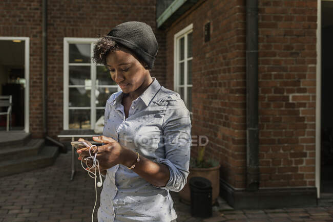 Усміхнена жінка використовує смартфон зовні будинку — стокове фото